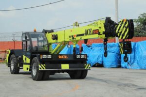 A construction crane lifting heavy materials at a job site with a caution sign stating "Avoid Crane Rental Mistakes" in bold letters. The background shows an active construction project with workers ensuring safe crane operation.